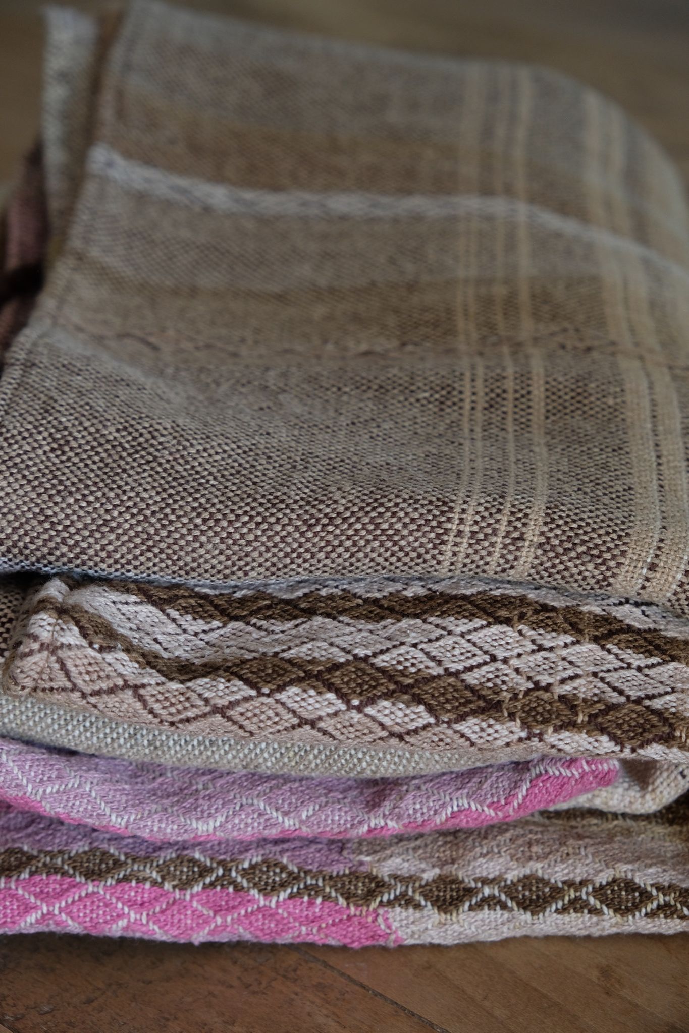 Handwoven fabric in soft shades of grey, pink, yellow and earth laying on a wooden floor