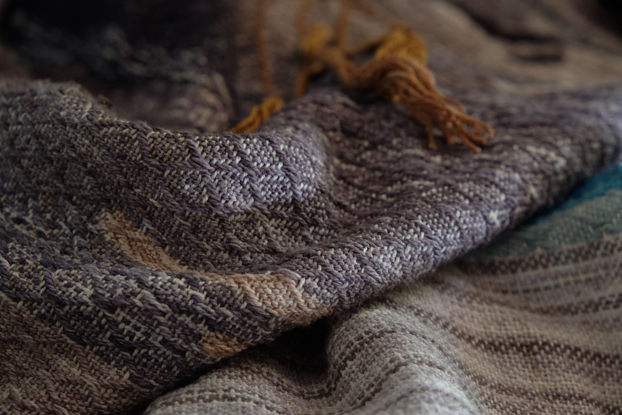 a small owl detail on A handwoven, diamond pattern shawl in blues, grey, black, brown, pink and green laying on a wooden floor