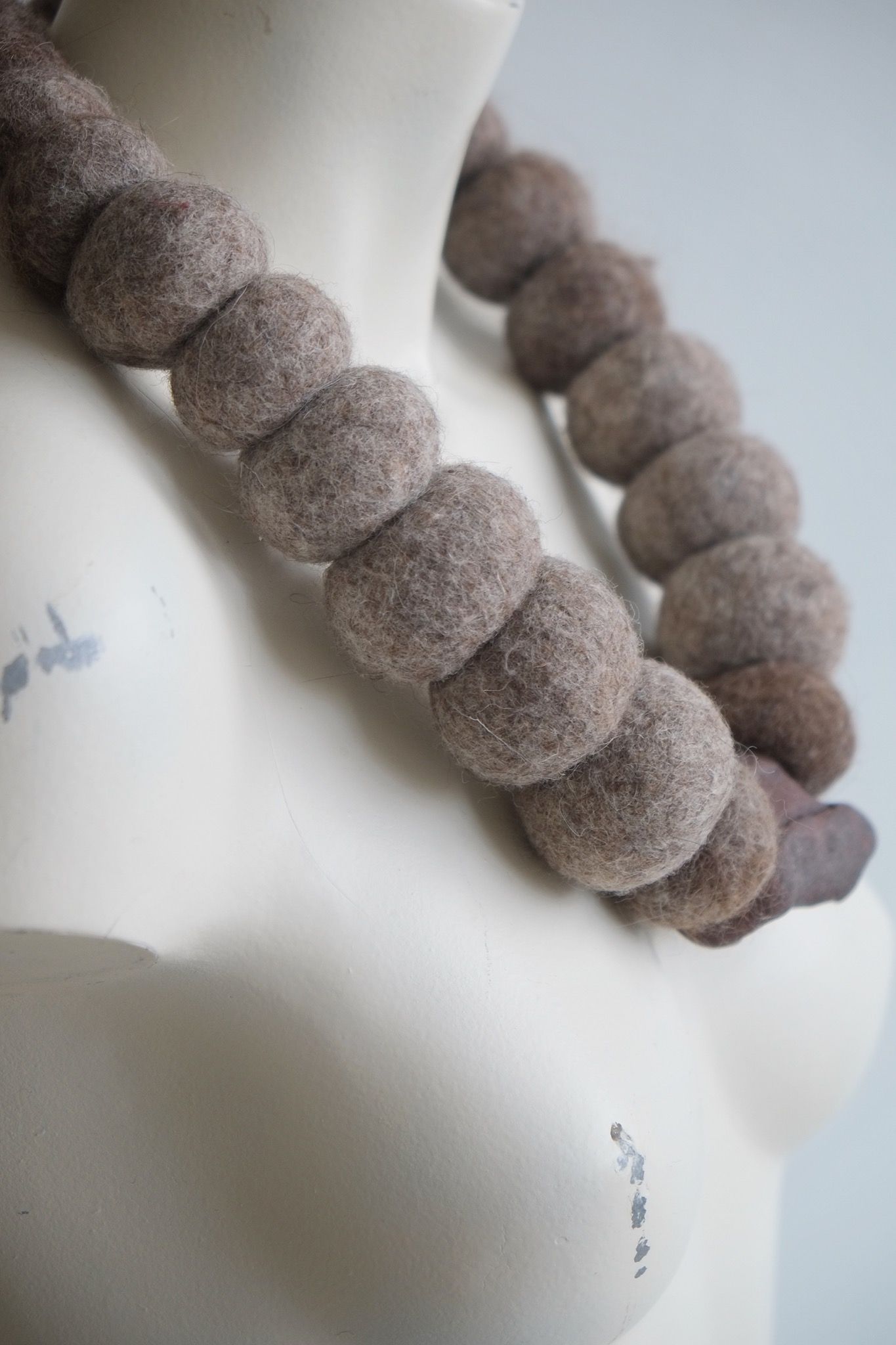 A sculptural necklace of grey wool felt spheres and an iron stone centerpiece rest on a white mannequin 