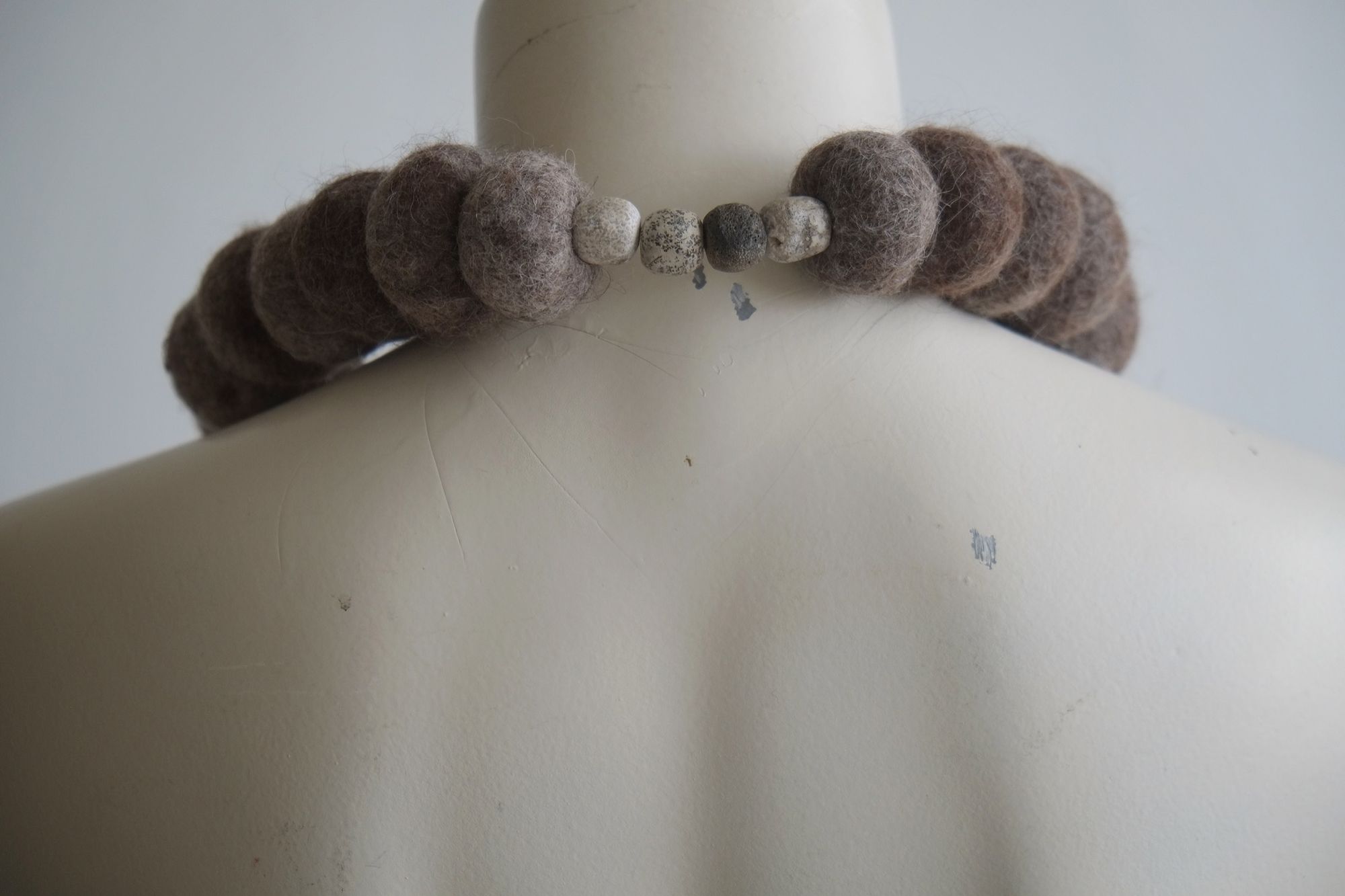 A sculptural necklace of grey wool felt spheres and an iron stone centerpiece rest on a white mannequin 