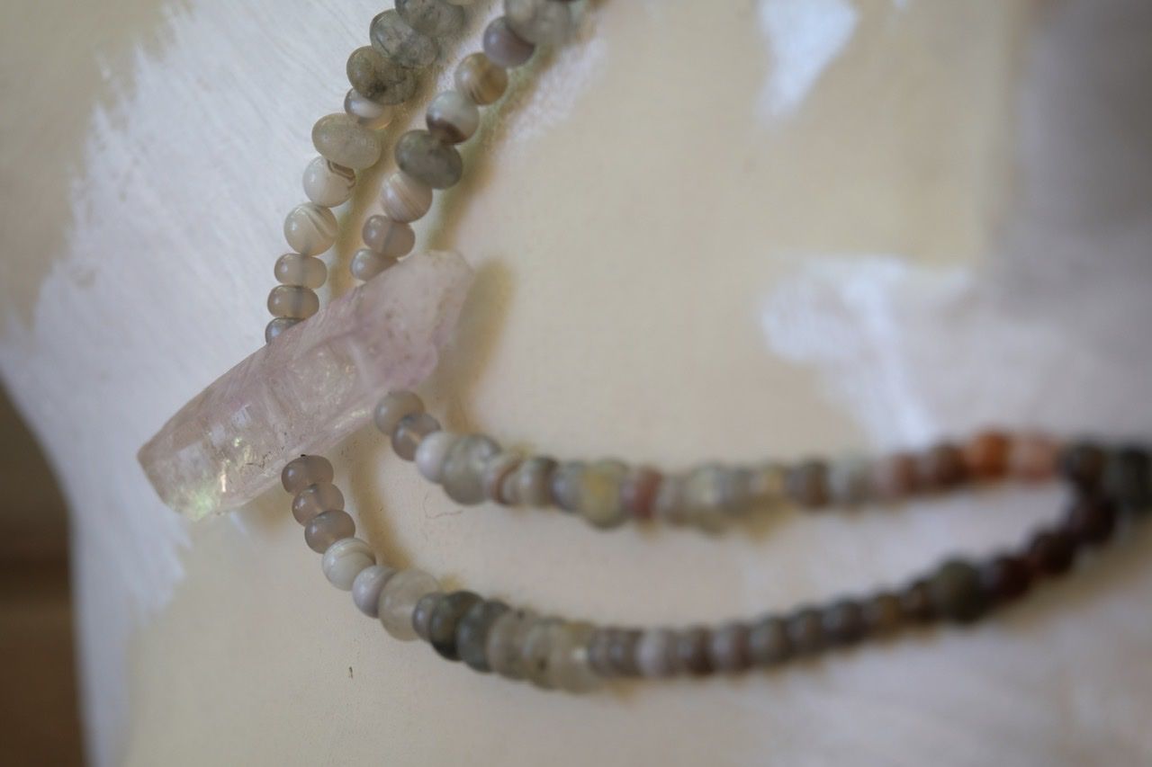 A white female shaped mannequin wearing a necklace made of light purple amethyst and grey White quartz 