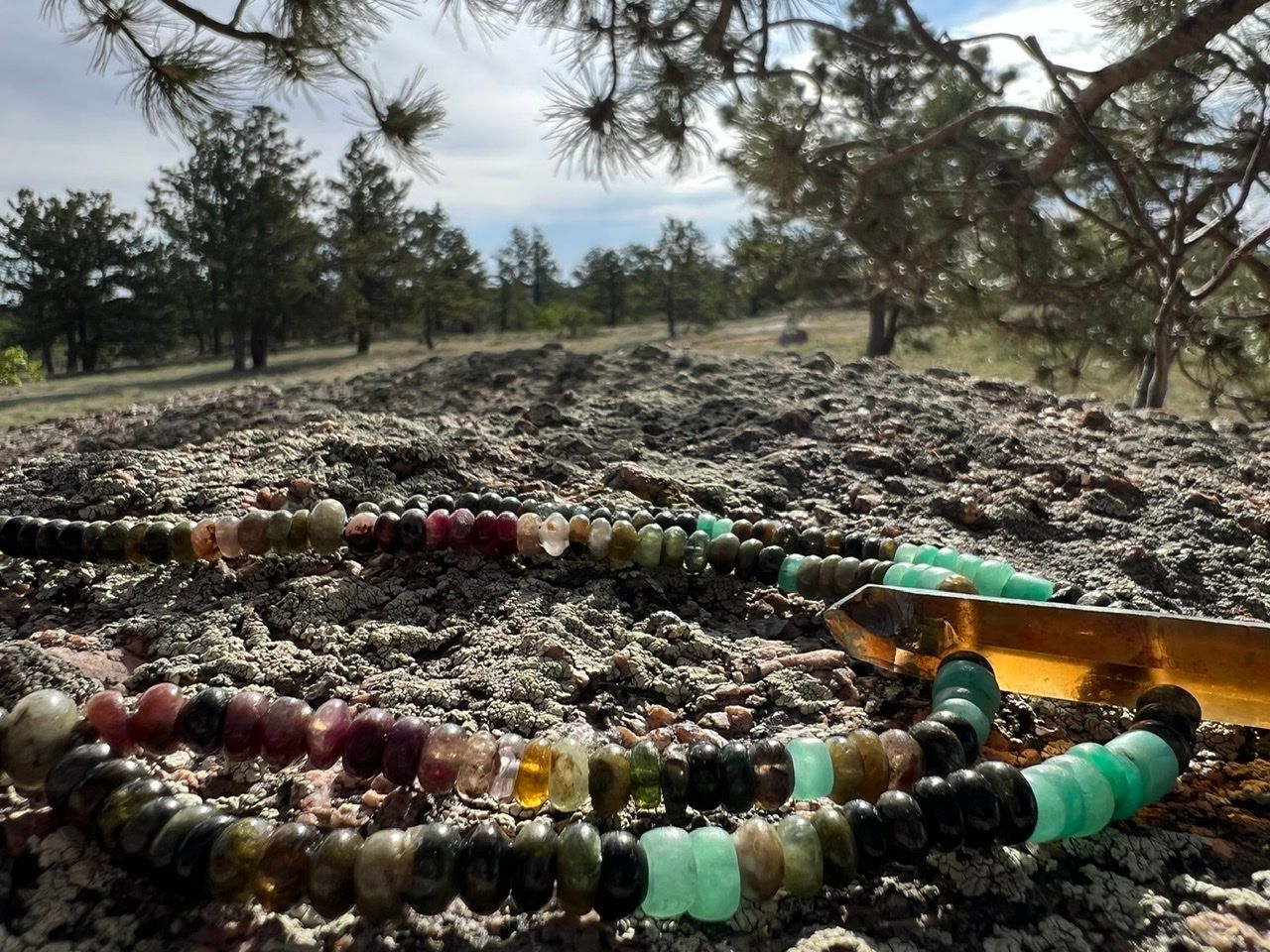 A precious stone necklaces in Greens, pinks, blues and yellows lays on a lichen covered stone