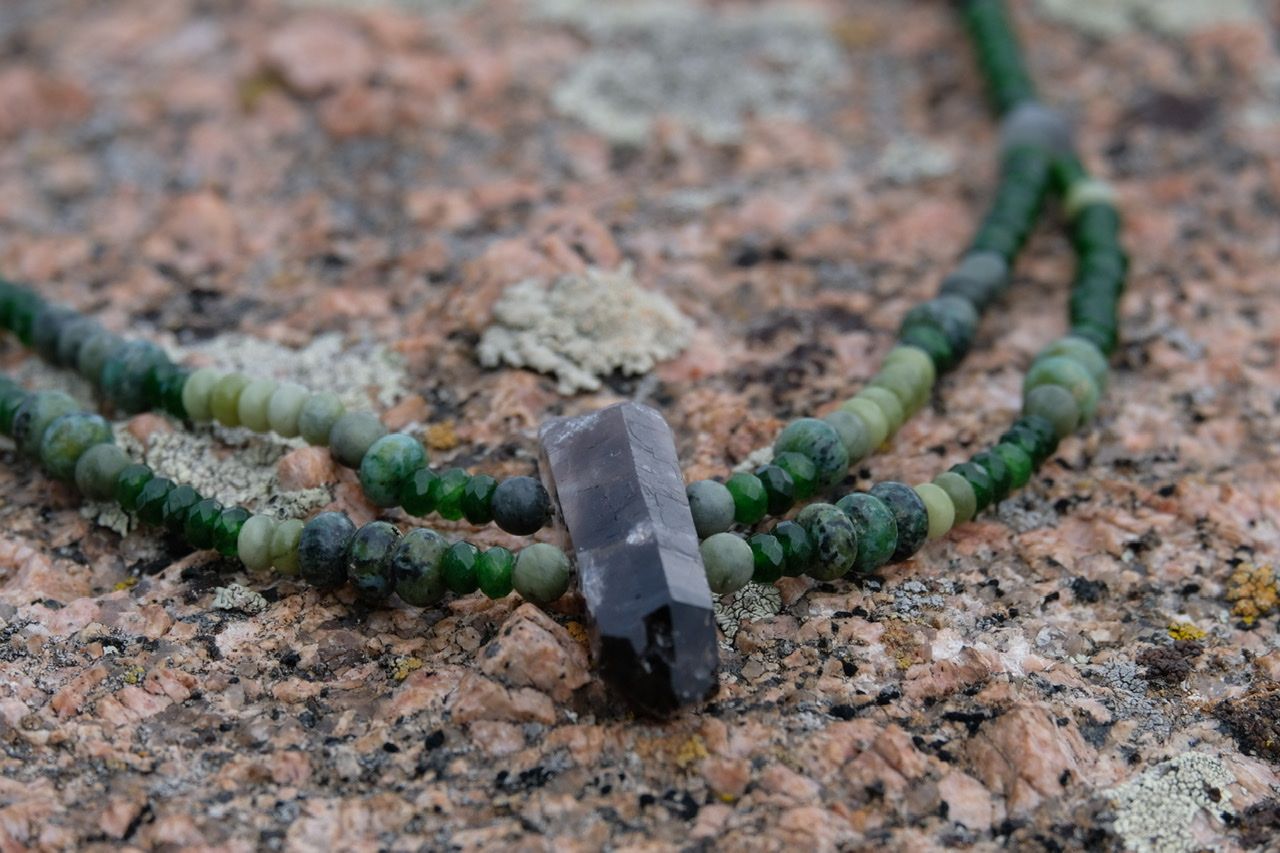Grey smoky Quartz and green stone necklace laying on a lichen covered granite rock