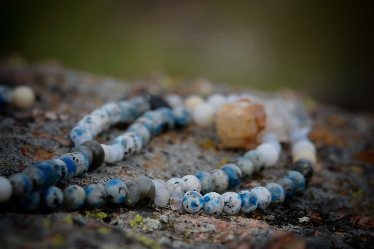 Blue, white, cream and pale yellow Stone and crystal necklace laying on a lichen covered rock