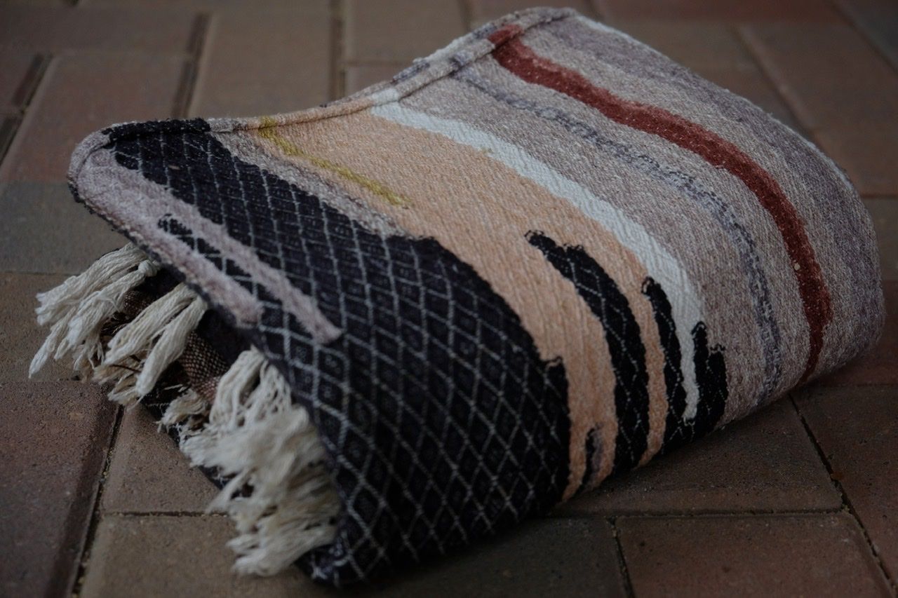Handwoven blue, yellow, grey, black, tan and maroon fabric laying folded on a brick floor