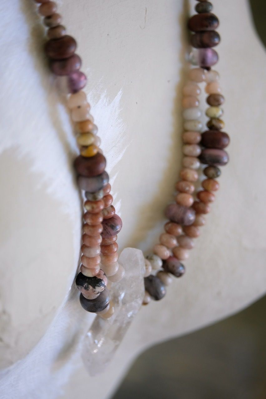 A crystal and stone necklace of pinks, cream, tan, white and grey rests on a white painted mannequin 