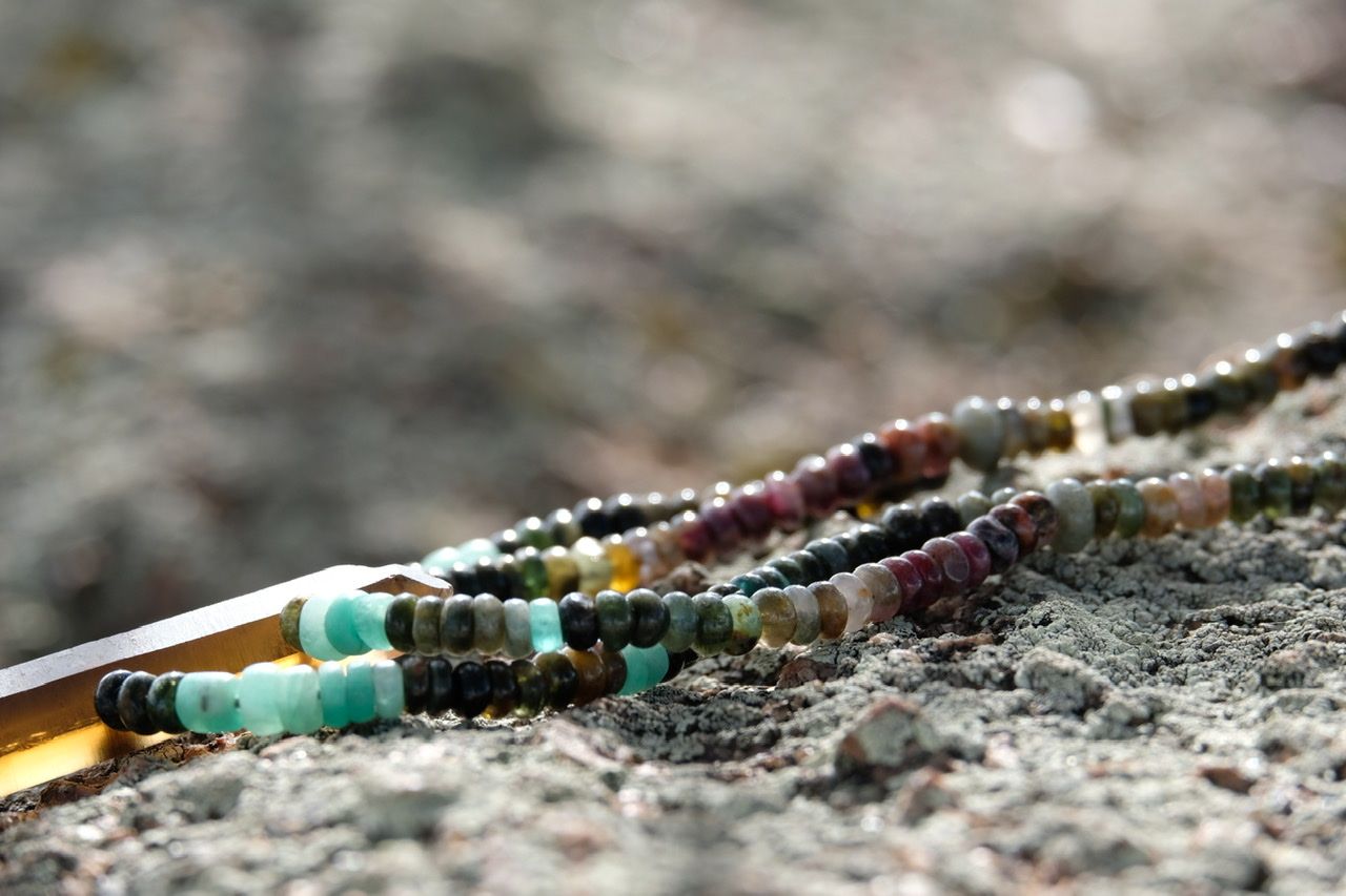 A precious stone necklaces in Greens, pinks, blues and yellows lays on a lichen covered stone