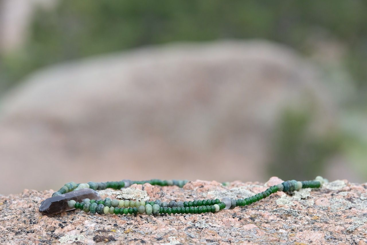 Grey smoky Quartz and green stone necklace laying on a lichen covered granite rock