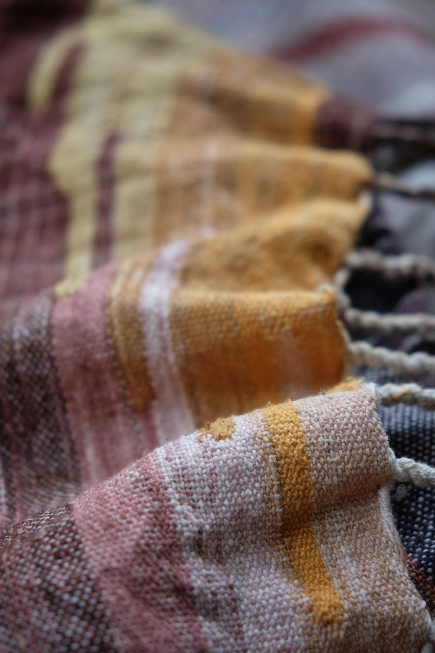 Handwoven blue, yellow, grey, black, tan and maroon fabric laying on a brick floor