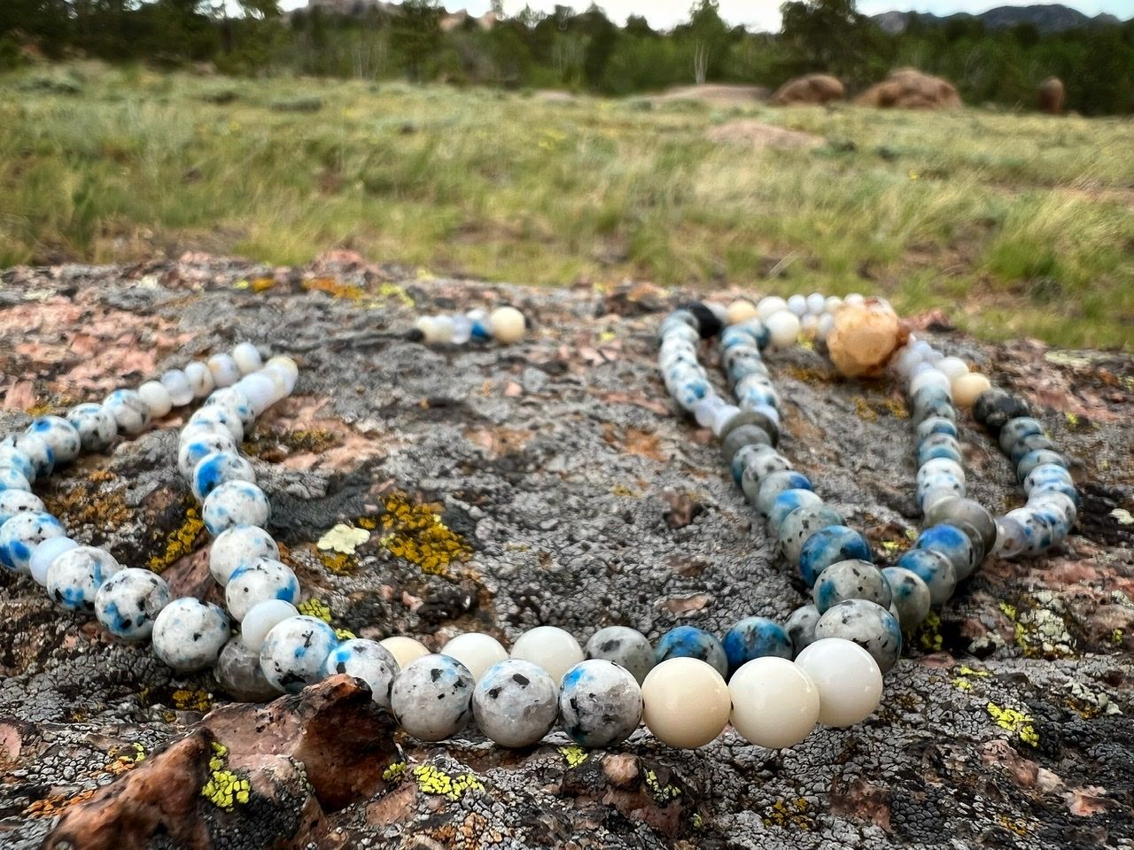 Blue, white, cream and pale yellow Stone and crystal necklace laying on a lichen covered rock