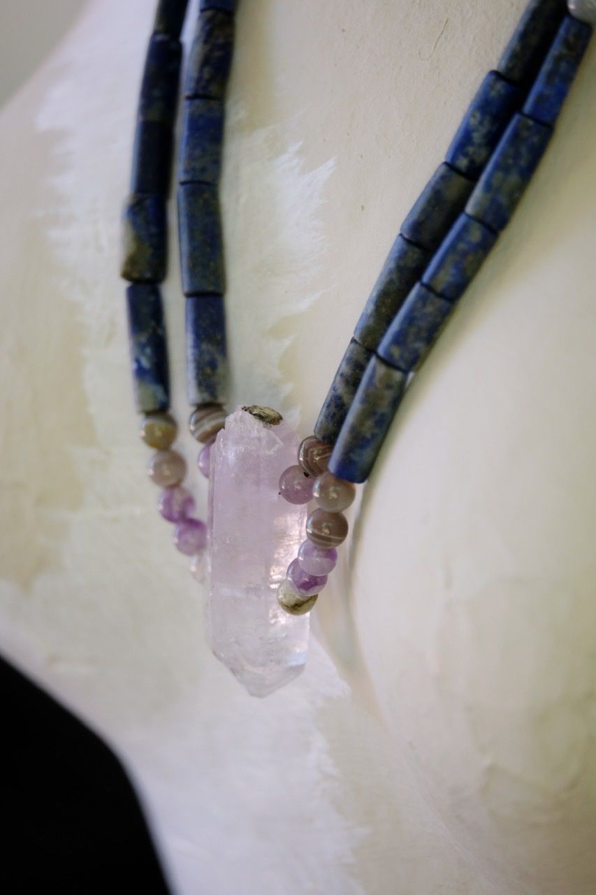 A blue lapiz and purple amethyst necklace rests on a white painted mannequin