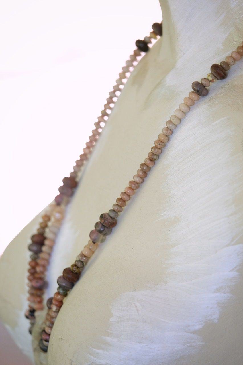A crystal and stone necklace of pinks, cream, tan, white and grey rests on a white painted mannequin 