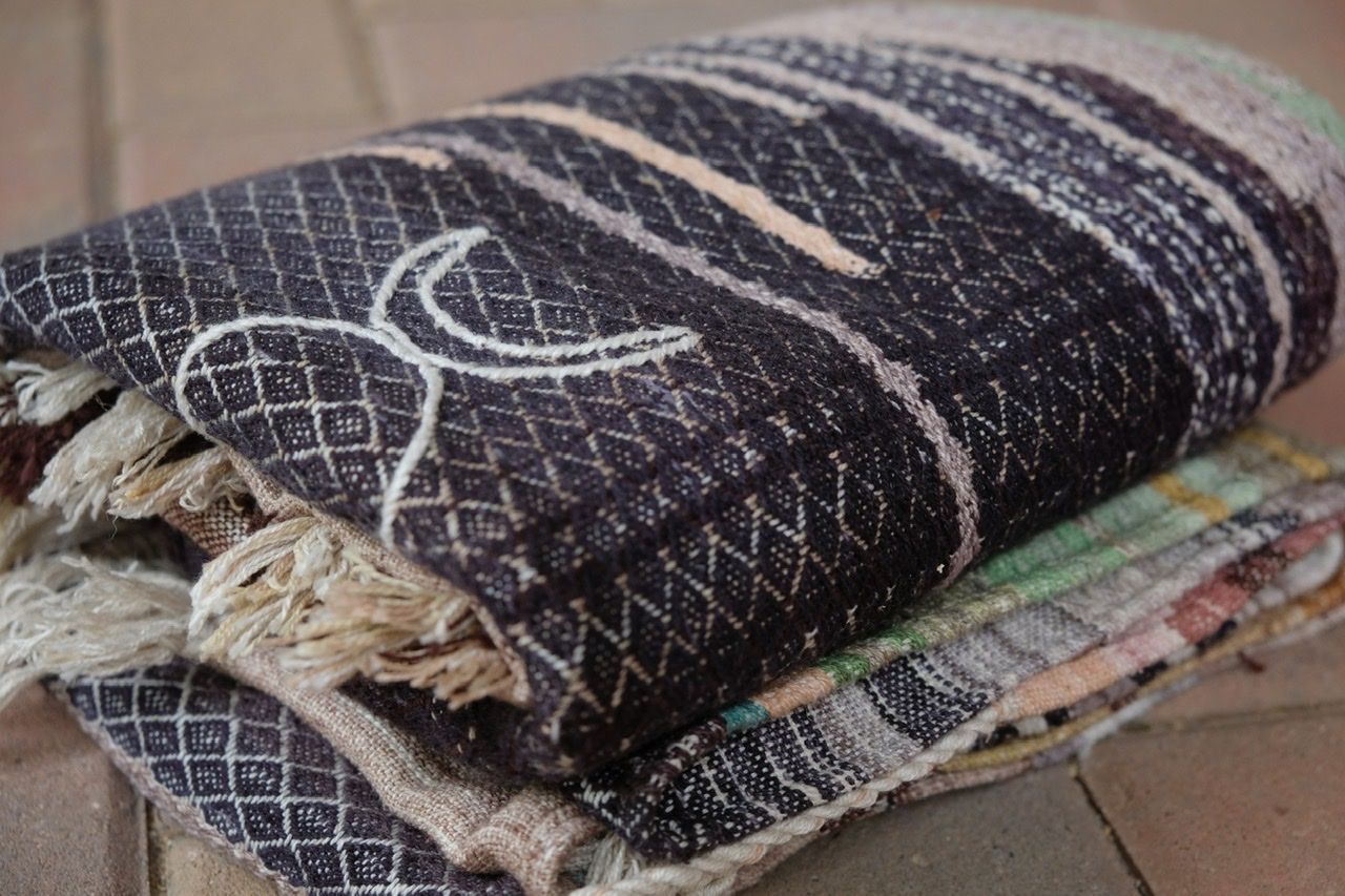 Handwoven blue, yellow, grey, black, tan and maroon fabric laying folded on a brick floor