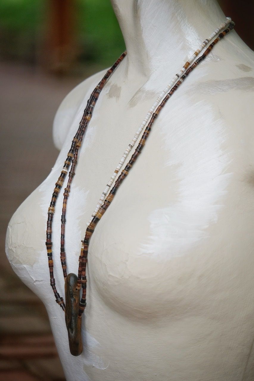 A necklace of dark brown petrified wood with white, gold, tan and brown shell beads On a white mannequin 