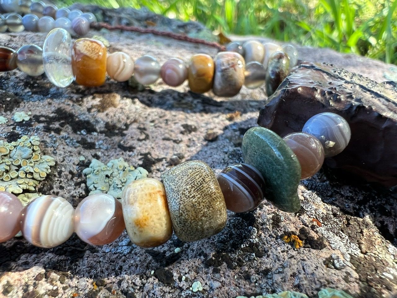 A necklace of earth tone agates and fossils rests on a lichen covered Boulder 