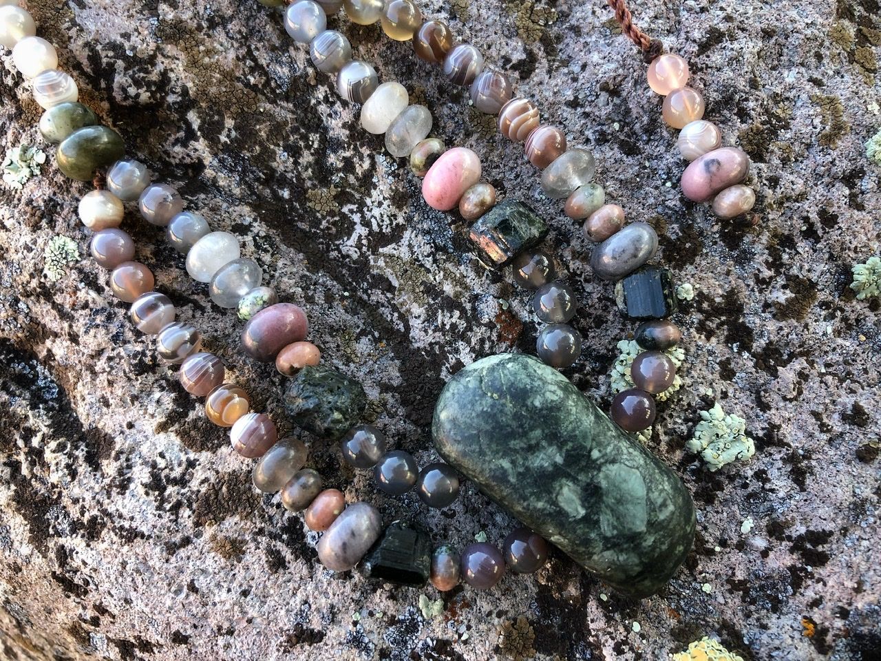 A pink, white, tan and green stone necklace rests on a lichen covered Boulder