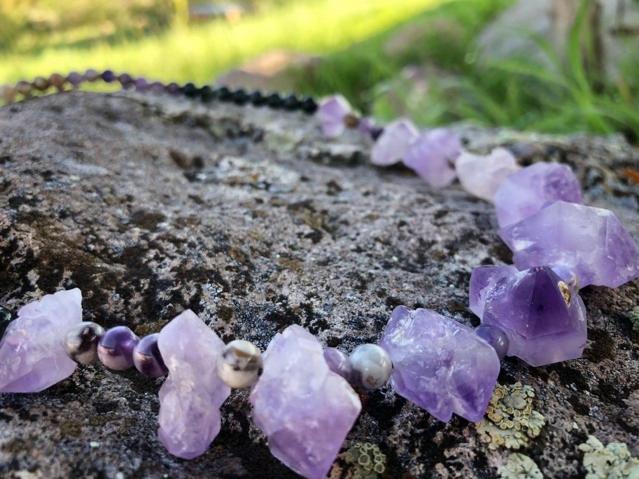 A purple amethyst crystal and black cats eye necklace rests on a lichen covered Boulder