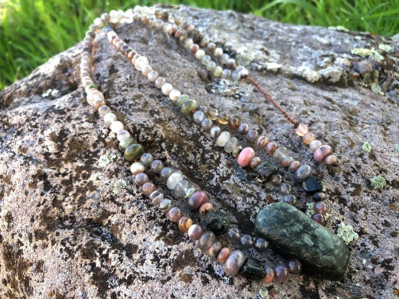 A pink, white, tan and green stone necklace rests on a lichen covered Boulder