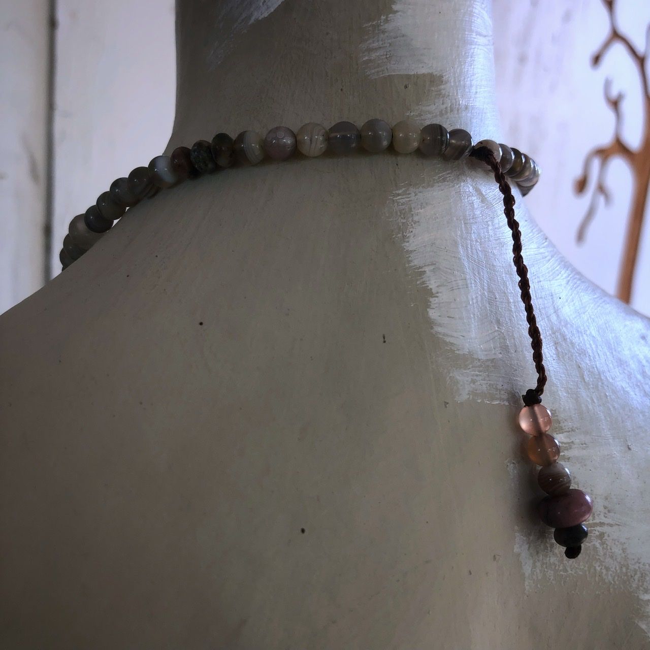 A two strand crystal and stone necklace rests on a white mannequin on a wood table with sunflowers in the background 