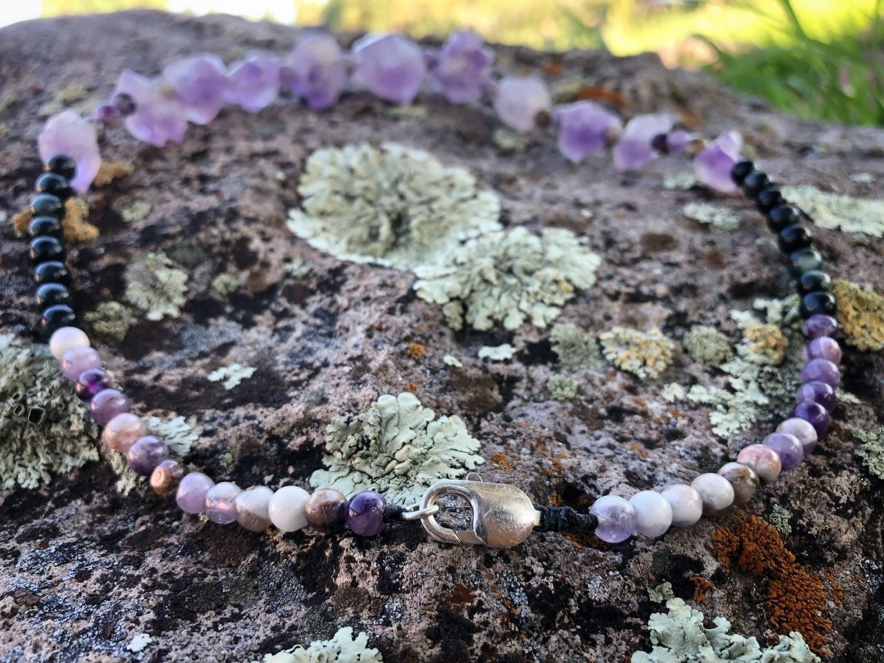 A purple amethyst crystal and black cats eye necklace rests on a lichen covered Boulder