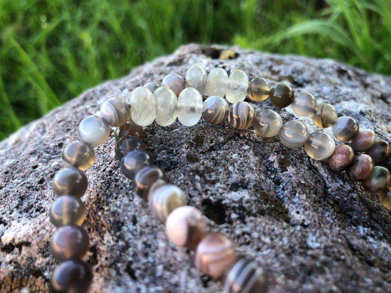 A pink, white, tan and green stone necklace rests on a lichen covered Boulder