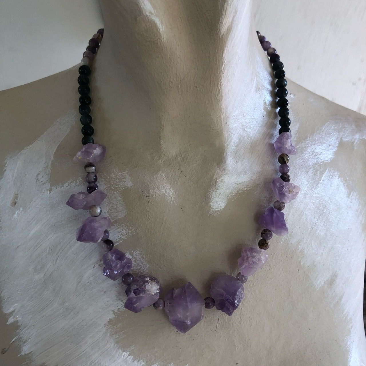 A amethyst crystal necklace rests on a white mannequin on a wood table with sunflowers in the background 