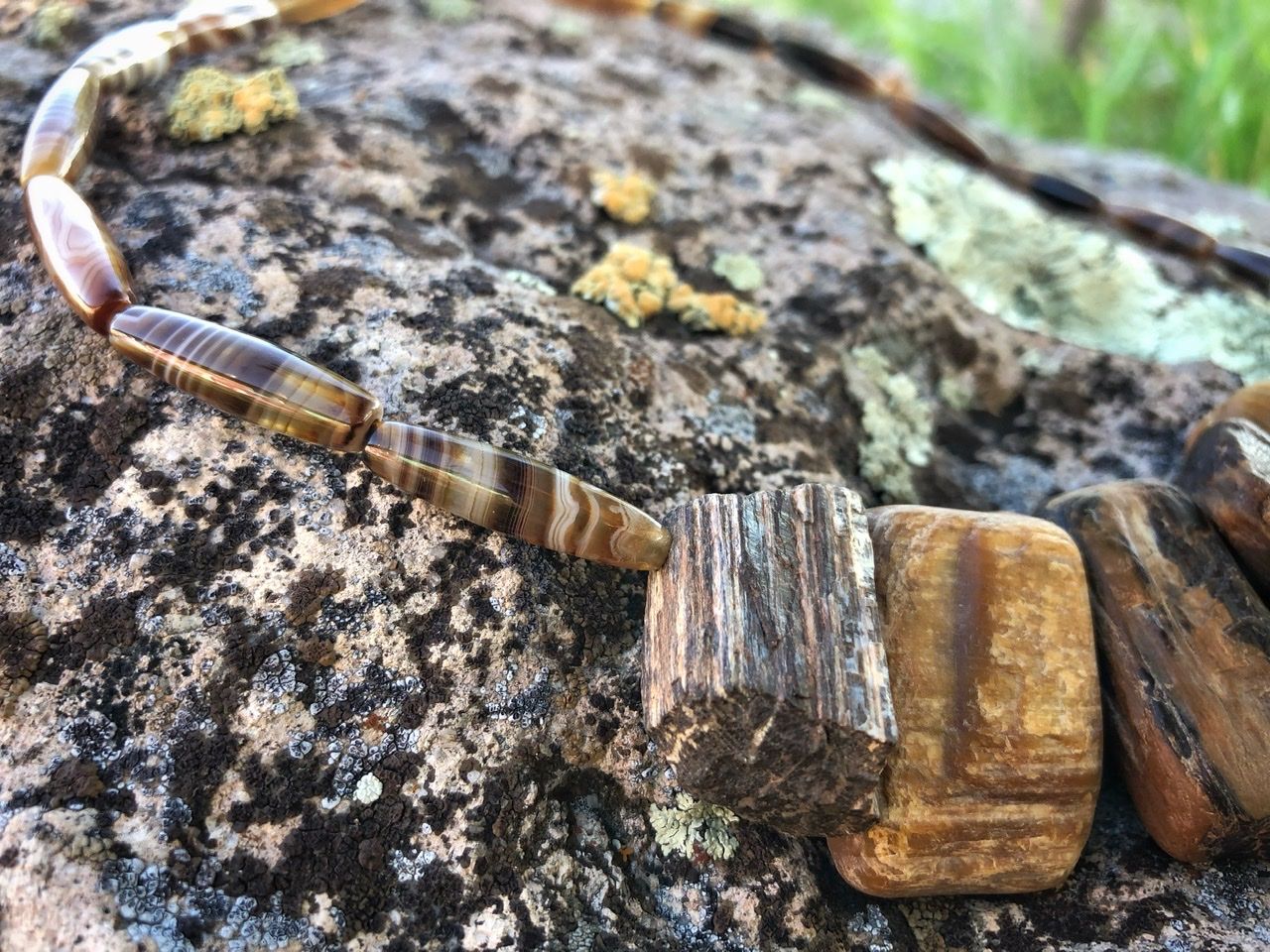 A petrified wood and brown banded agate necklace rests on a lichen covered Boulder