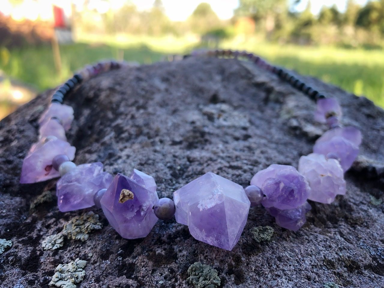 A purple amethyst crystal and black cats eye necklace rests on a lichen covered Boulder