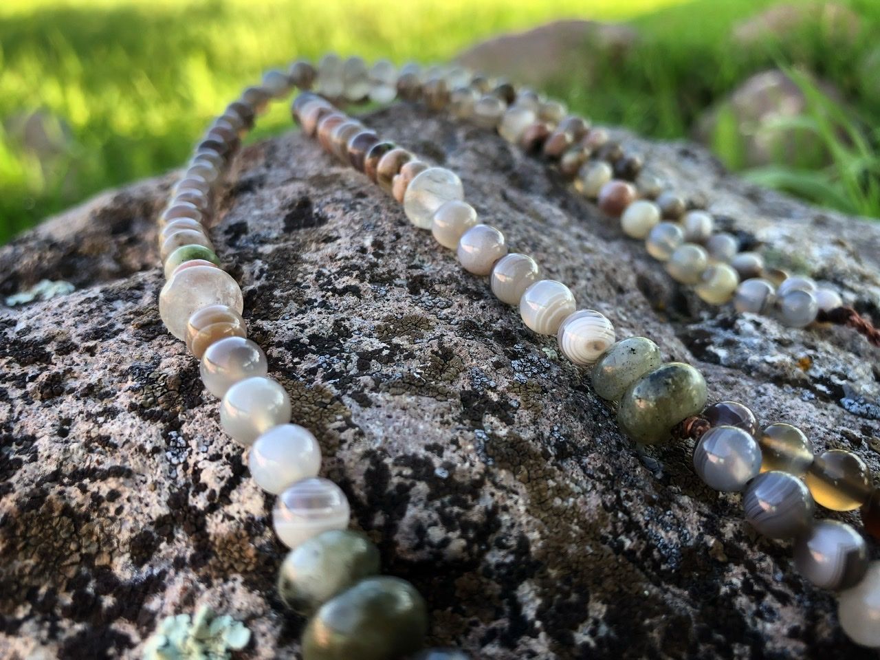 A pink, white, tan and green stone necklace rests on a lichen covered Boulder