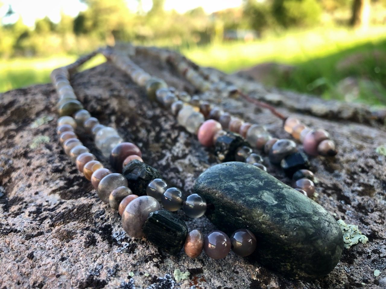 A pink, white, tan and green stone necklace rests on a lichen covered Boulder