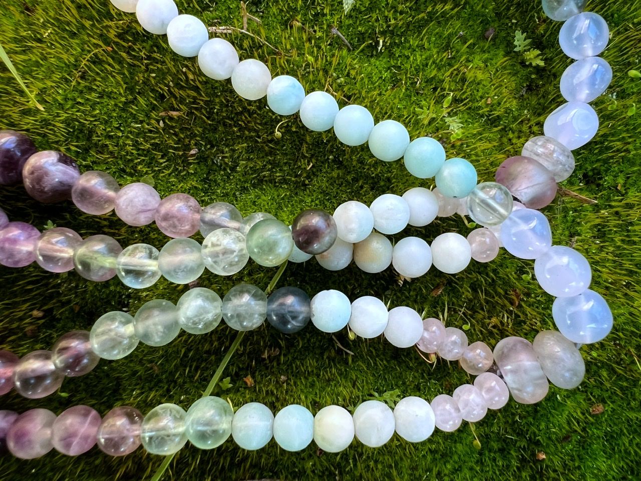 A necklace of clear, pink and grey Quartz, purple amethyst, green fluorite and blue chalcedony rests on lush green moss