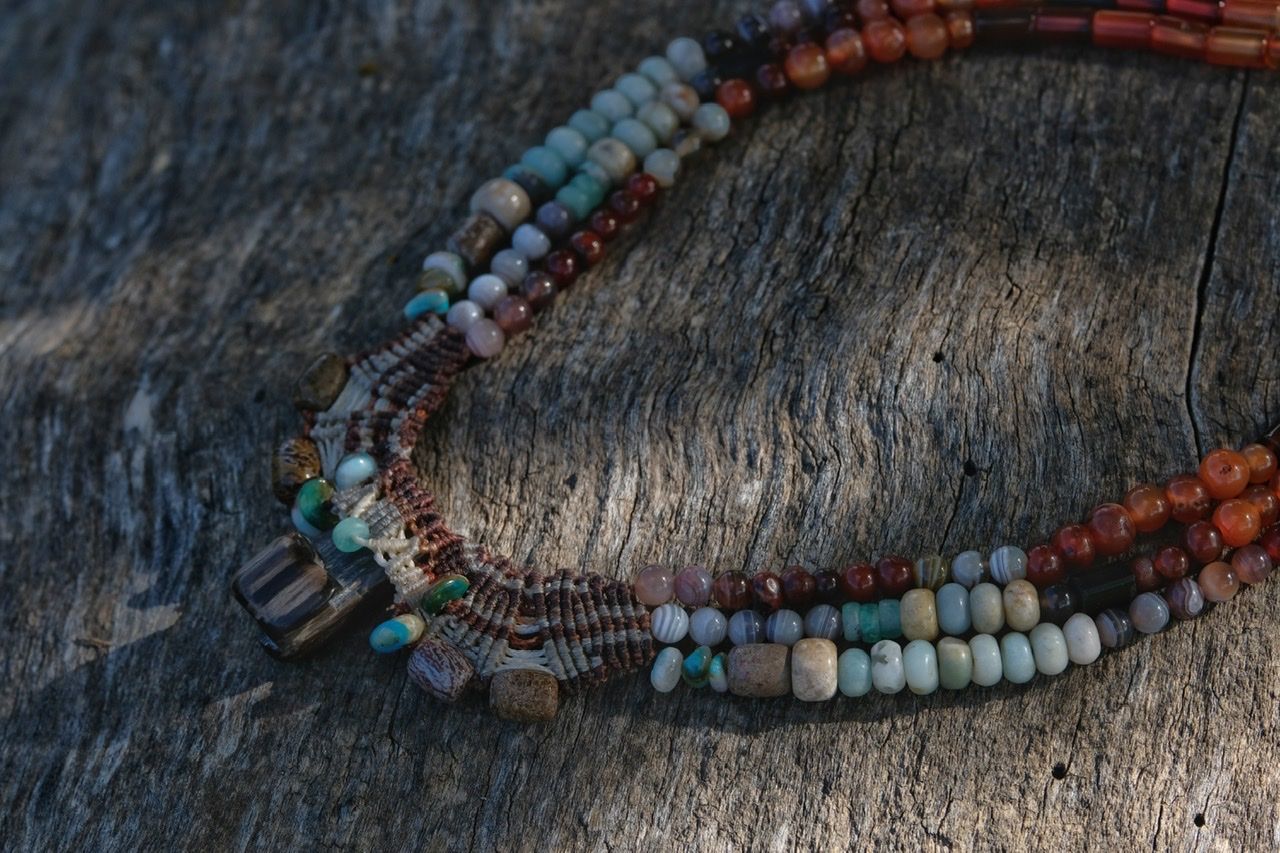 Knotwork and stone necklace in emerald green, brown, yellow, blue, red and purple, laying on a grey log