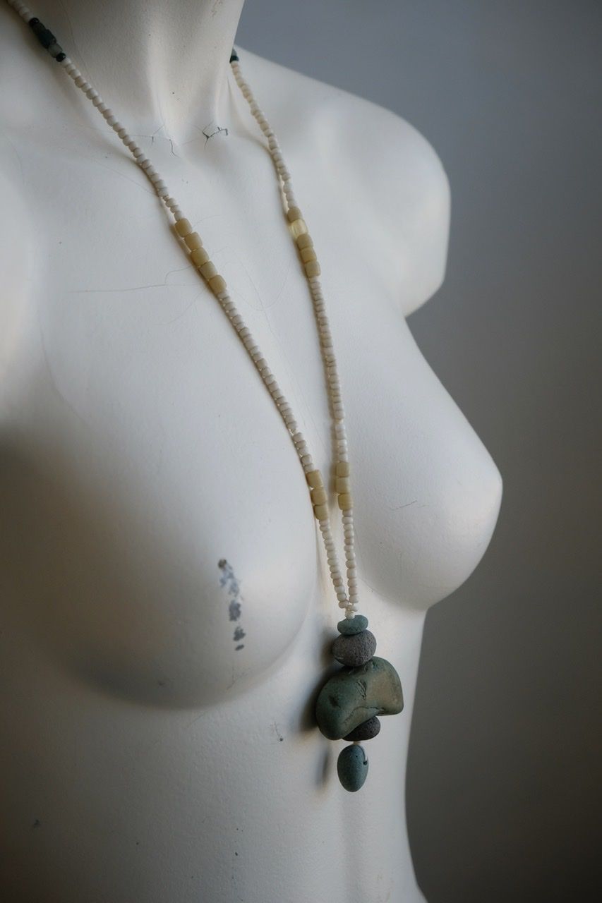 A white colored female form mannequin wears a sculptural necklace of blue green river tumbled stones and white glass beads