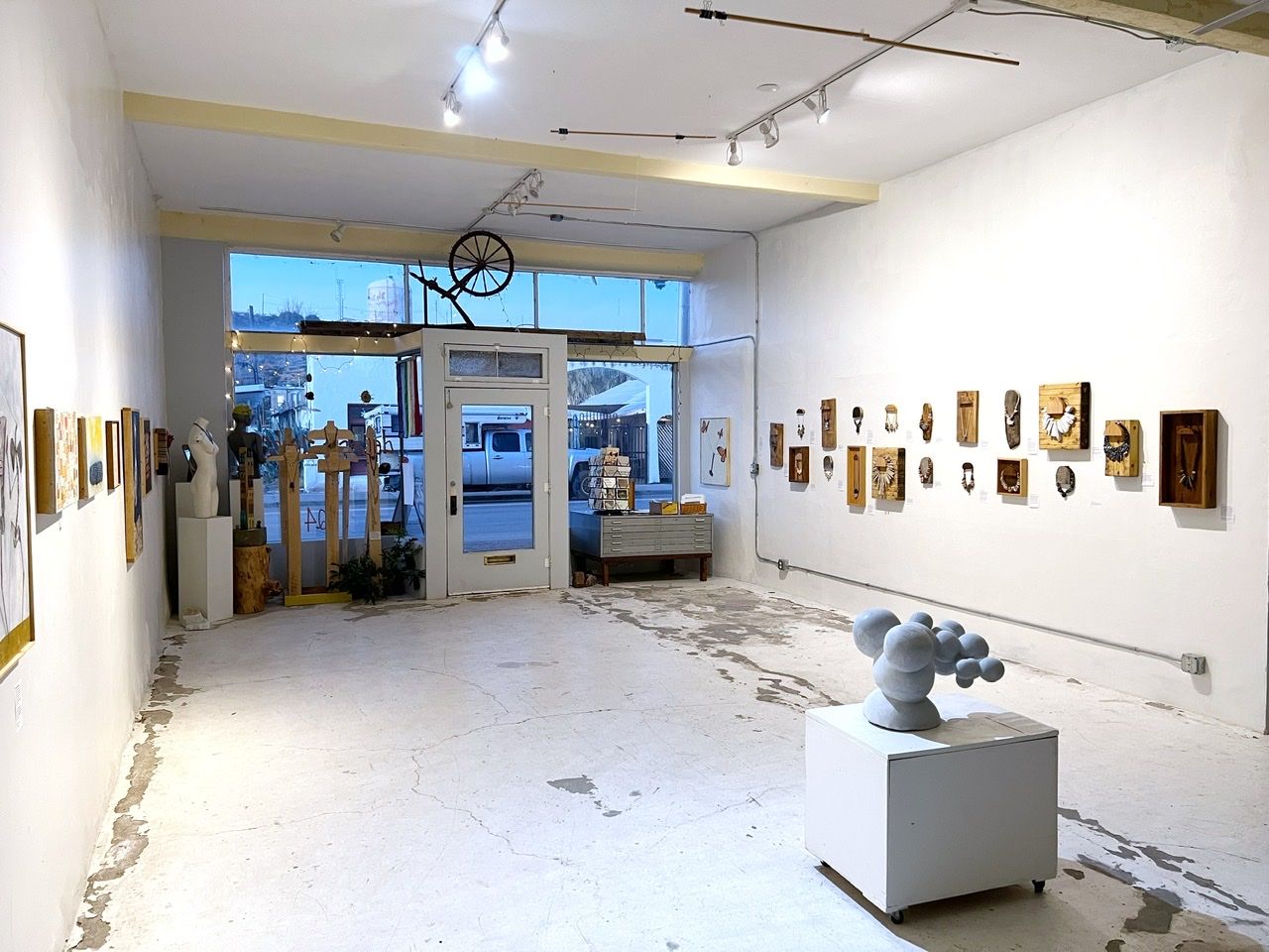 the interior view of a gallery with a marble sculpture of a molecule on the floor and art on the white walls