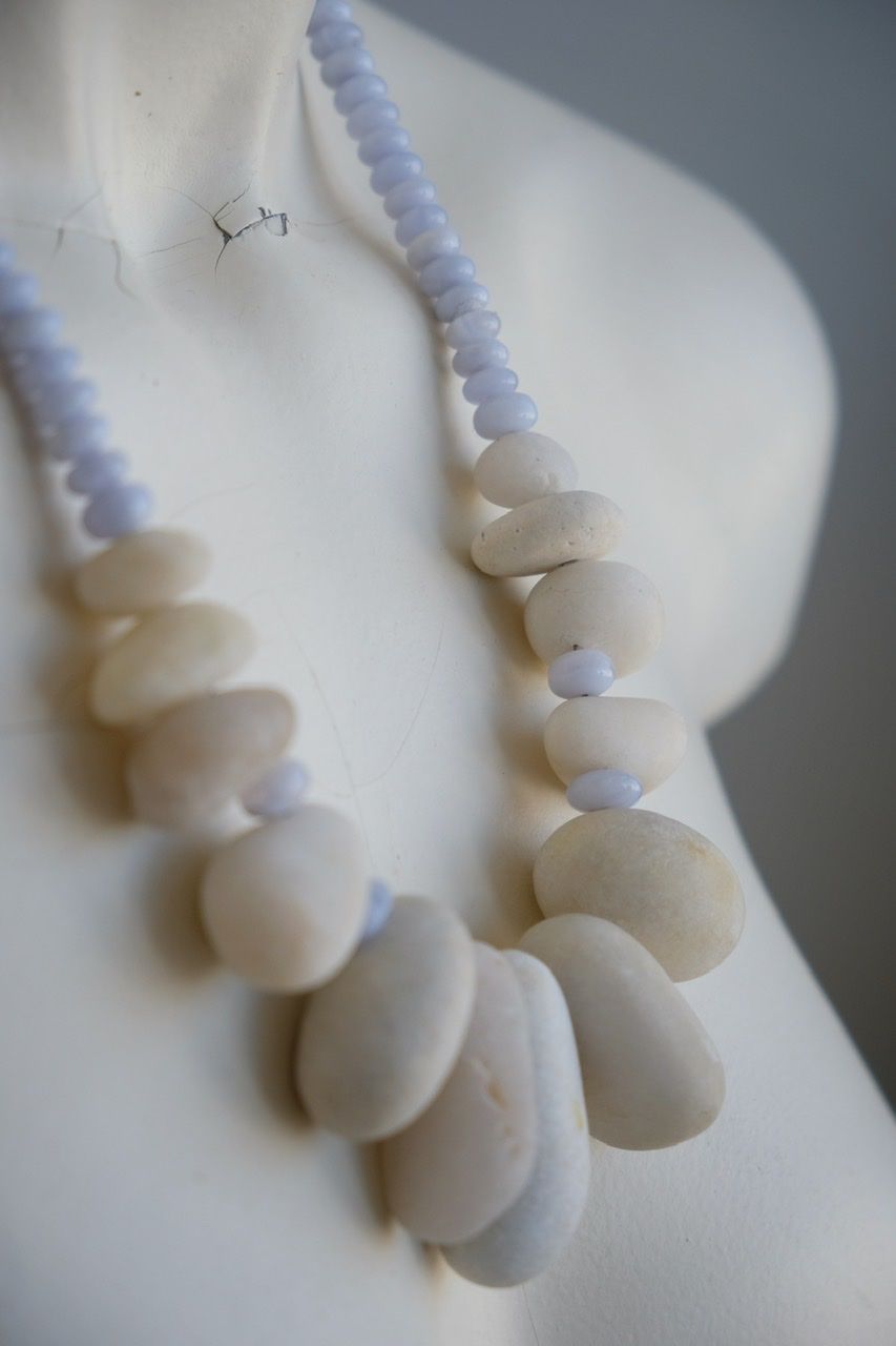 A white colored female form mannequin wears a sculptural necklace of white stone orbs and crystalline blue chalcedony beads