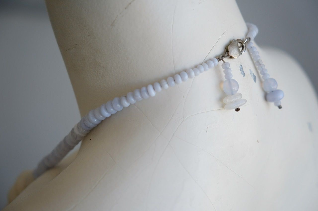 A white colored female form mannequin wears a sculptural necklace of white stone orbs and crystalline blue chalcedony beads