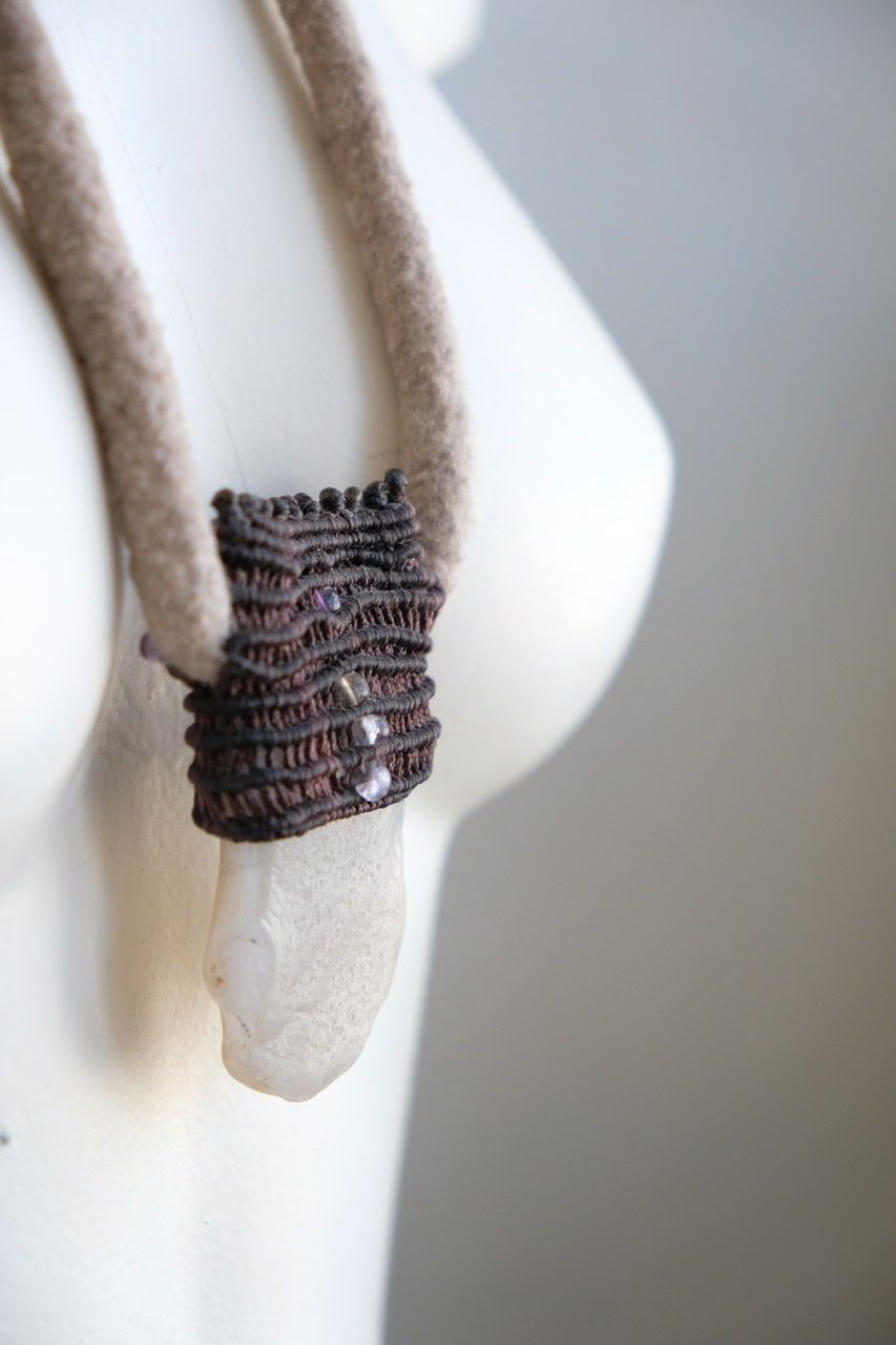 A white colored female form mannequin wears a sculptural necklace of a light grey felted cord, dark purple basket with a white chalcedony stone