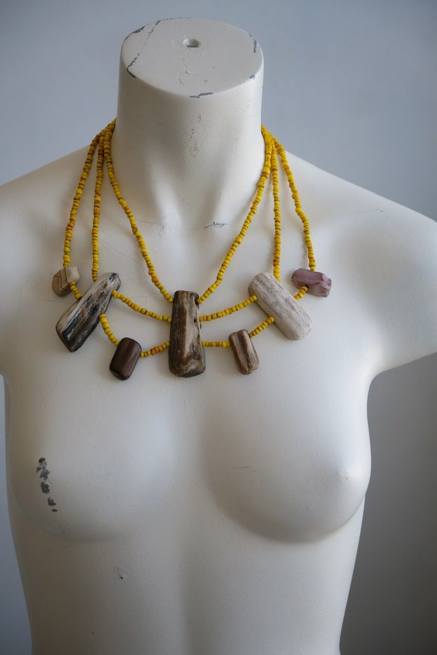 A white colored female form mannequin wears a three strand sculptural necklace of petrified wood and yellow glass beads