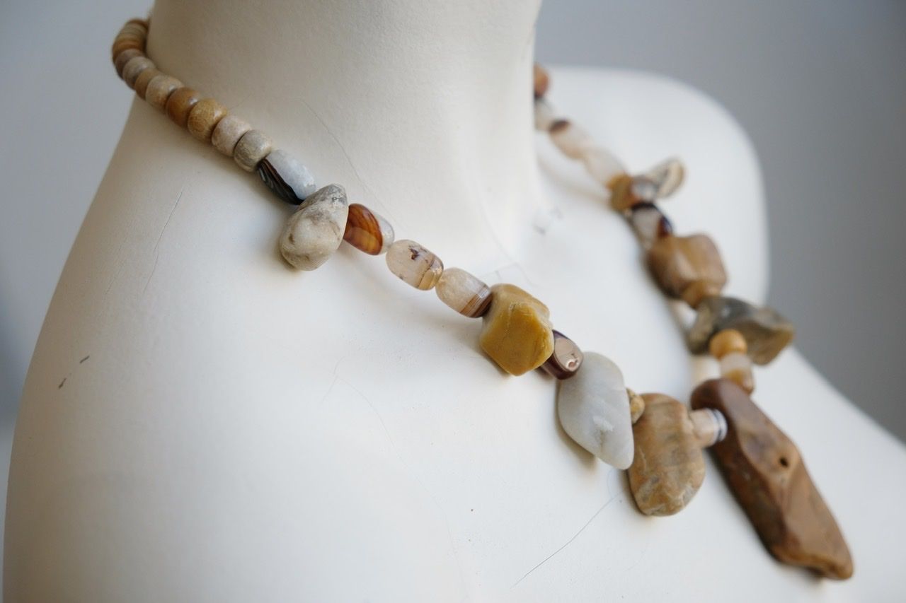 A white color female form mannequin wears a sculptural stone necklace in toffee, cream and yellow colors 