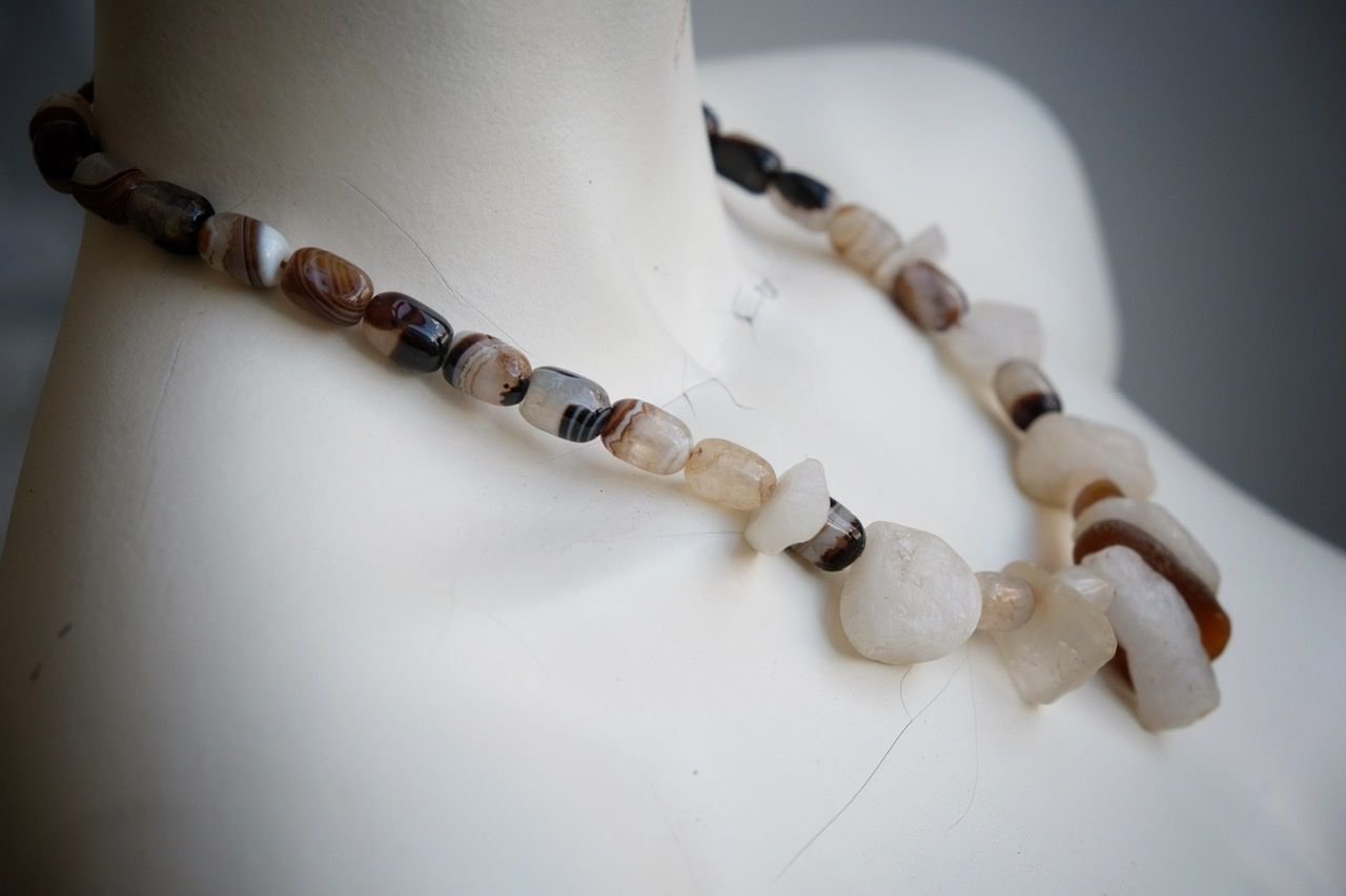 A white colored female form mannequin wears a white, clear and brown necklace of agate, Quartz and tumbled glass