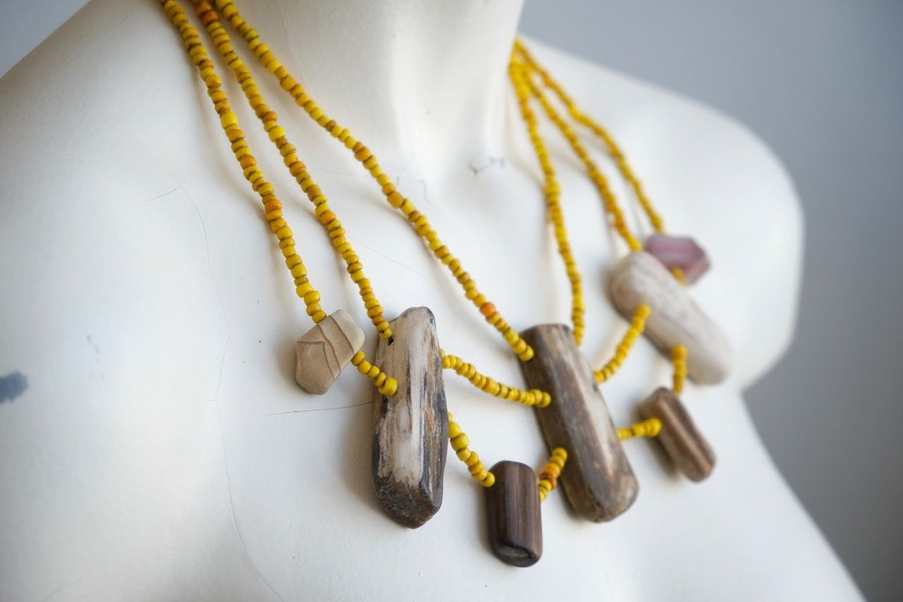 A white colored female form mannequin wears a three strand sculptural necklace of petrified wood and yellow glass beads