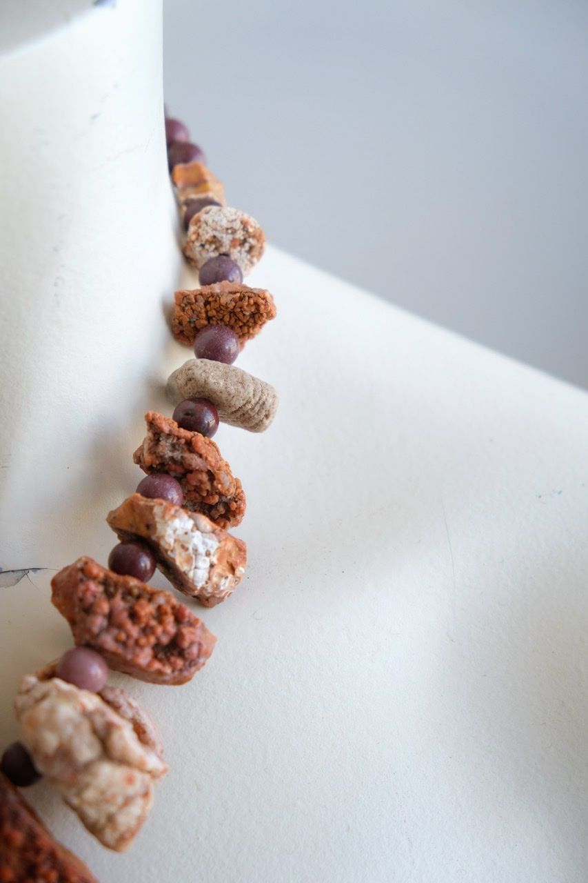 A white colored female form mannequin wears a snort necklace of orange botryoidal stones with yellow and purple jasper beads