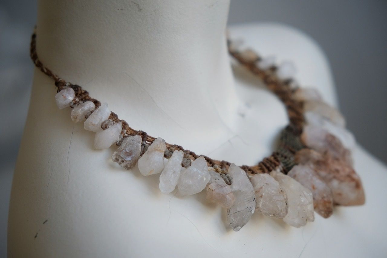 A white colored female form mannequin wears a sculptural necklace of rough quartz points and brown and green knotwork