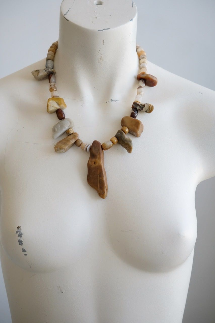 A white color female form mannequin wears a sculptural stone necklace in toffee, cream and yellow colors 