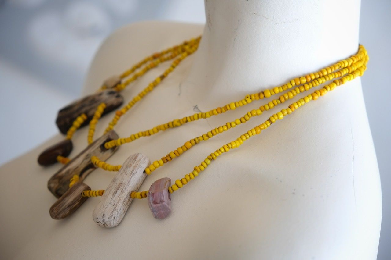 A white colored female form mannequin wears a three strand sculptural necklace of petrified wood and yellow glass beads