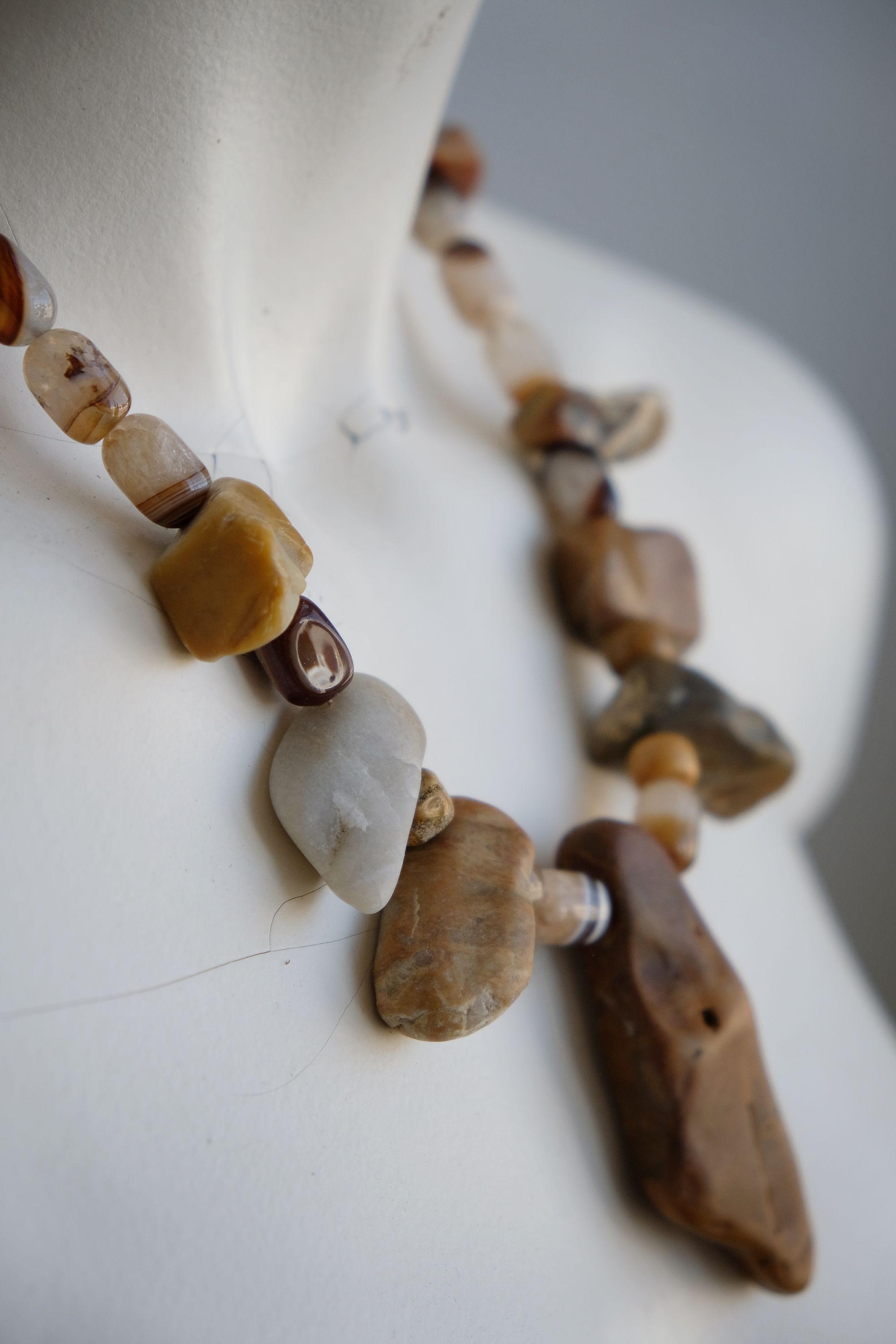 A white color female form mannequin wears a sculptural stone necklace in toffee, cream and yellow colors 