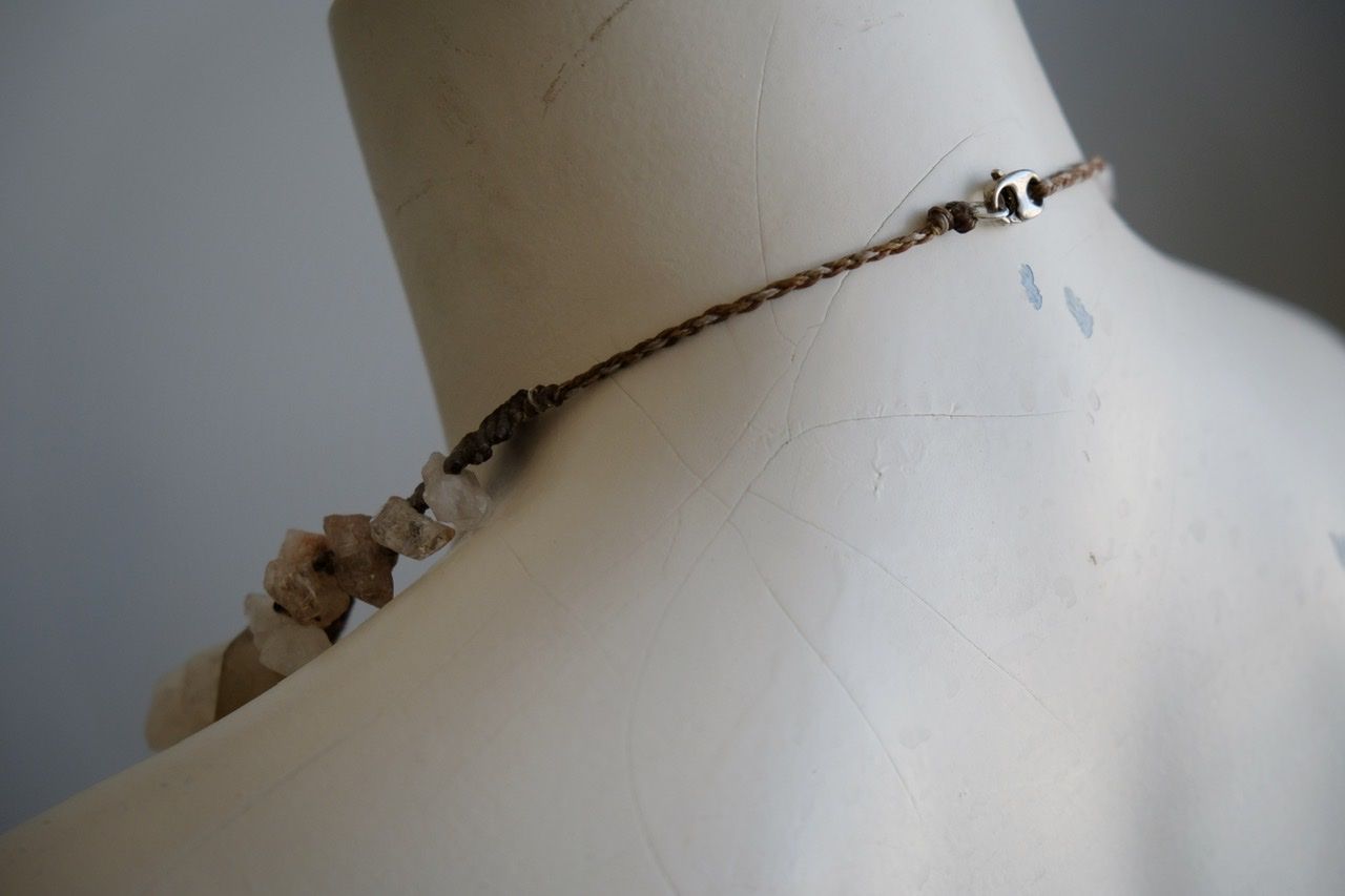A white colored female form mannequin wears a sculptural necklace of rough quartz points and brown and green knotwork