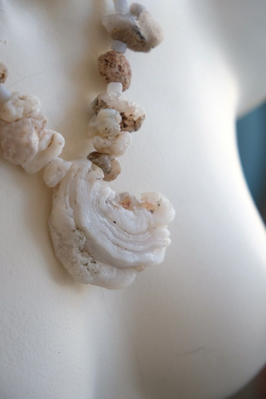 A white colored female form mannequin wears a necklace of white and blue botryoidal chalcedony