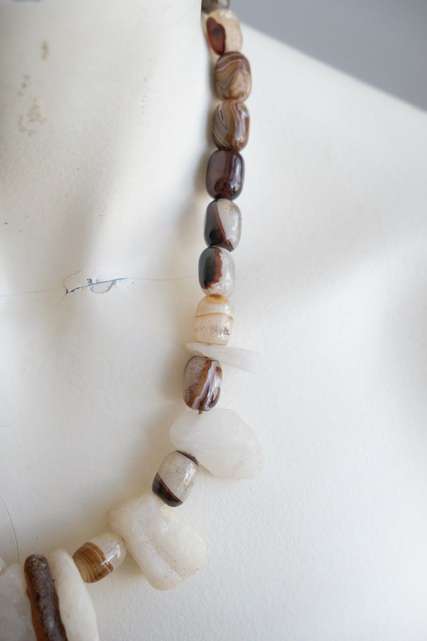 A white colored female form mannequin wears a white, clear and brown necklace of agate, Quartz and tumbled glass