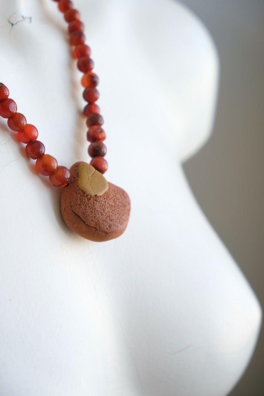 A white color female form mannequin wears a sculptural stone necklace in red, orange and yellow ochre colors 
